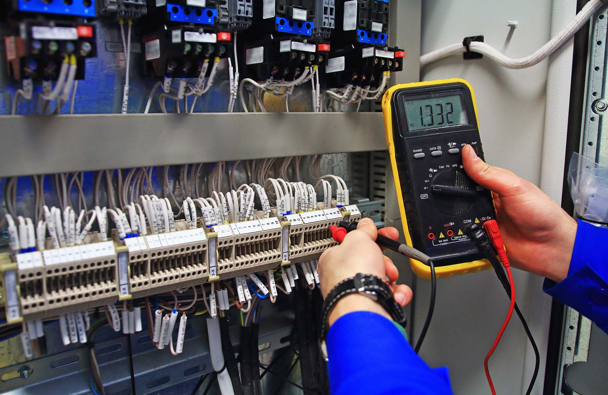 Engineer tests industrial electrical circuits with a multimeter in the control terminal box. Engineer tests the industrial electrical circuits with a multimeter in the control terminal box. Engineer`s hands with a multimeter close-up against background of terminal rows of automation panel.